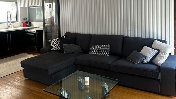 A modern living room with a sectional sofa, a glass coffee table, and a kitchen area with a refrigerator and stove. - Spacious stylish flat at acropolis area! (Athina)