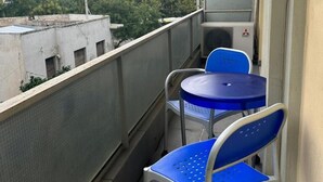 A balcony with two blue chairs and a small table, overlooking a cityscape with buildings and trees. - Spacious stylish flat at acropolis area! (Athina)