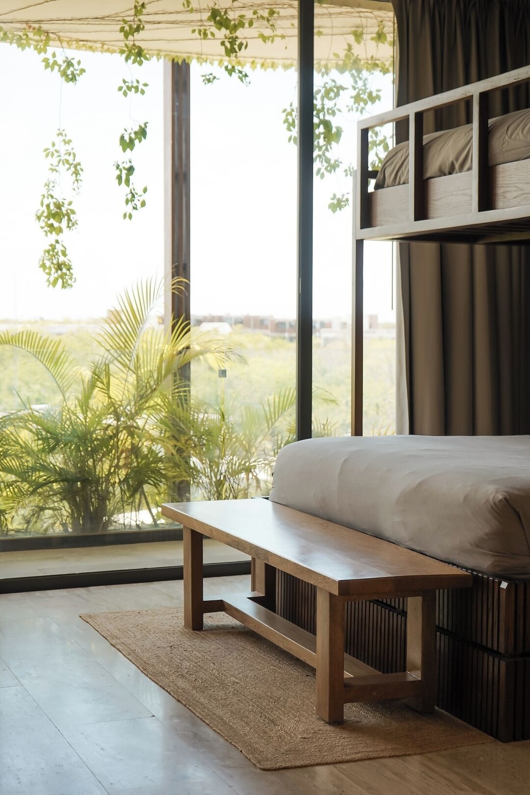 Ein Schlafzimmer mit großem Fenster, einem Bett, einer Bank und Blick auf Grün.