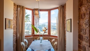 Uma sala de jantar com uma mesa posta para quatro pessoas, um vaso com flores e vista para montanhas através de grandes janelas.