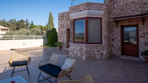 Um edifício de pedra com uma janela de canto e uma porta. Há cadeiras de vime e uma mesa com uma maçã vermelha.