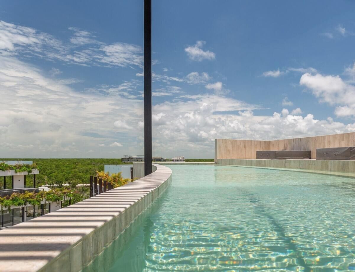 Ein moderner Infinity-Pool mit klarem Wasser, umgeben von einer Betonplattform und Blick auf eine üppige grüne Landschaft unter teilweise bewölktem Himmel.