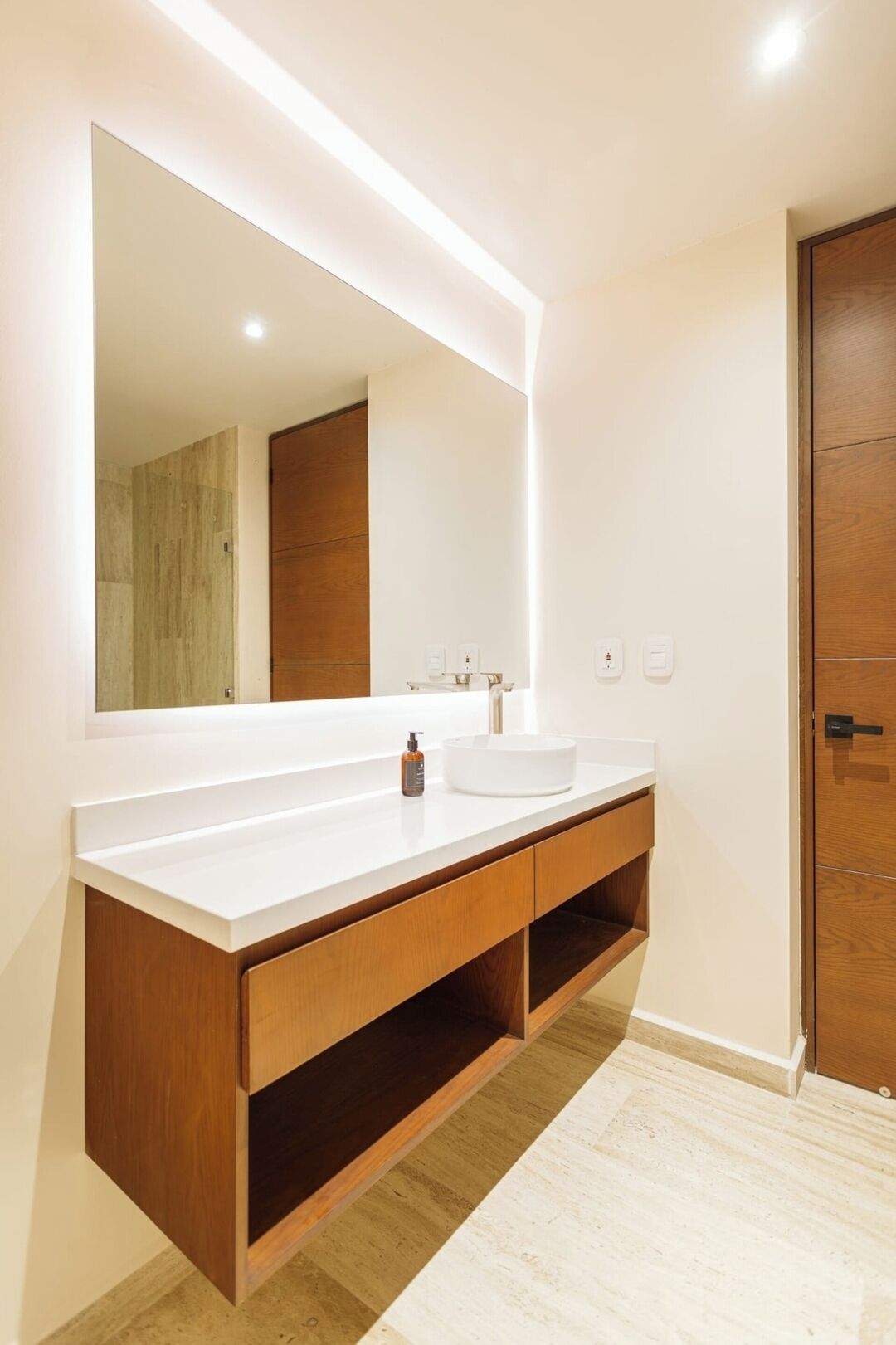 Une salle de bain moderne avec un grand miroir, un plan de toilette blanc, un meuble-lavabo en bois et une porte en bois.