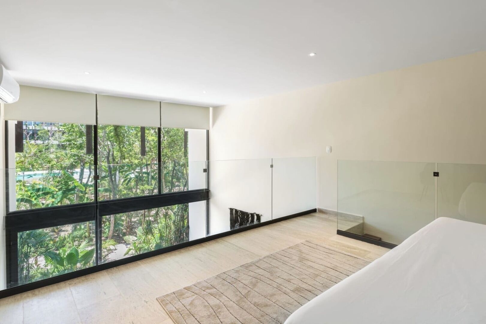 Une chambre moderne avec de grandes fenêtres, un lit et une vue sur la verdure environnante.