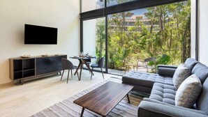A modern living room with a large window, a flat-screen TV, a sofa, a coffee table, and a dining area with chairs. - Spectacular Loft with gym, pool and beach shuttle (Tulum)
