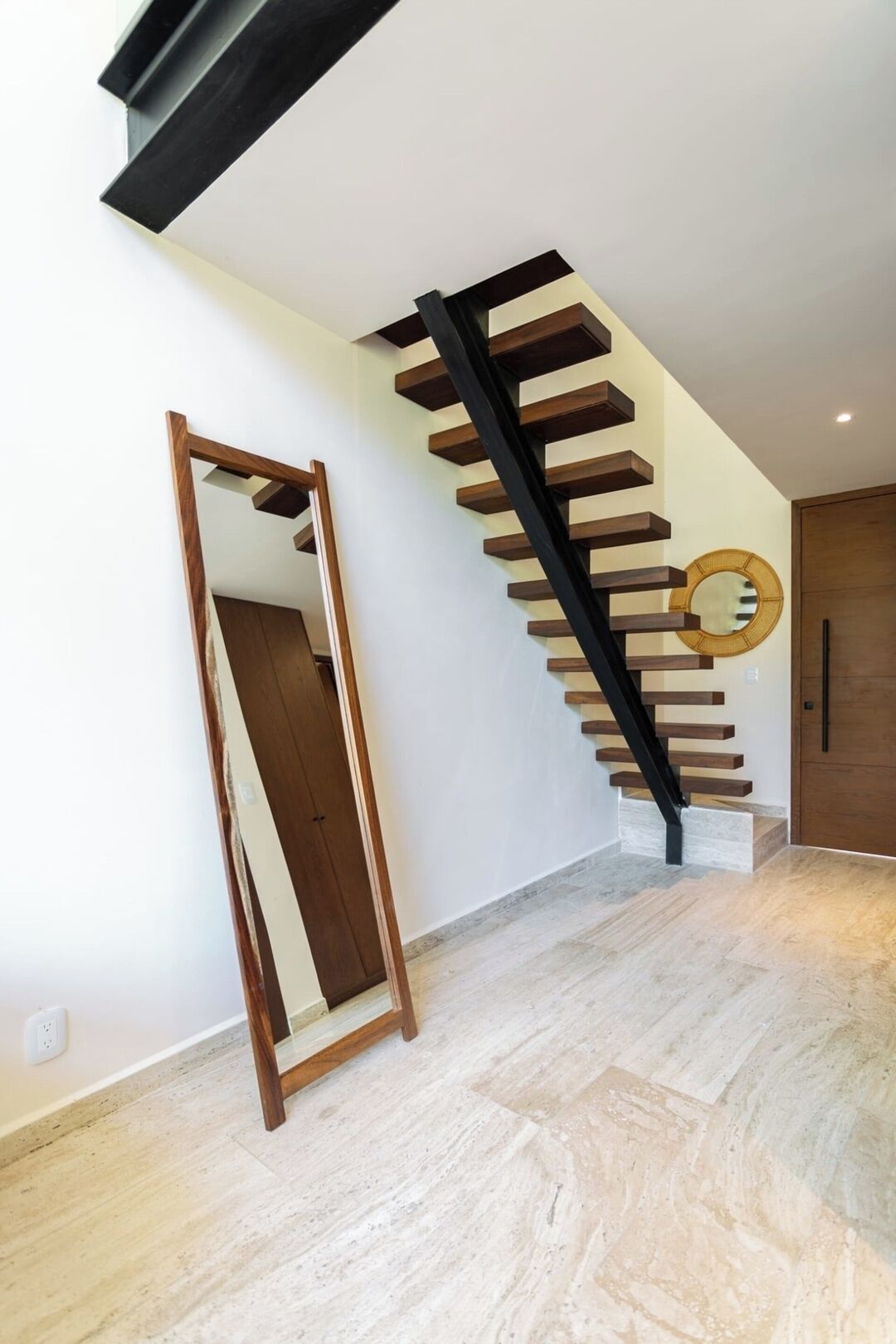 A modern interior with a staircase, a mirror, and a door.