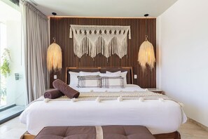 Ein modernes Schlafzimmer mit einem großen Bett, Holzvertäfelung, Wandbehängen aus Makramee und zwei Pendelleuchten.