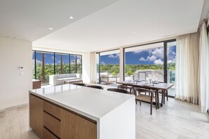 A modern kitchen with a large island, dining area with a table and chairs, and large windows offering a view of the outdoors. - Unique penhouse with private pool and jungle view! (Tulum)