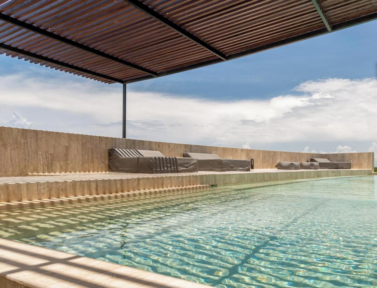 Une piscine dotée d’un espace couvert, de chaises longues et offrant une vue sur le ciel.