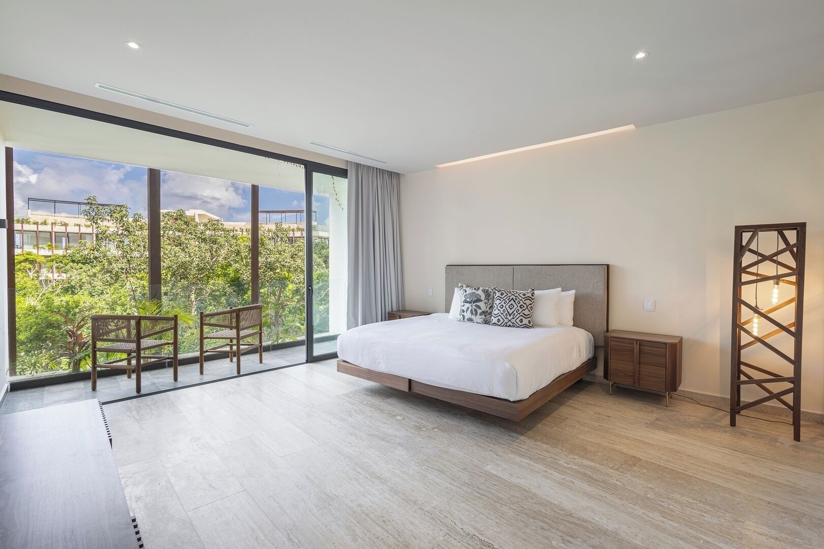 A modern bedroom with a large bed, a view of greenery, and a balcony.