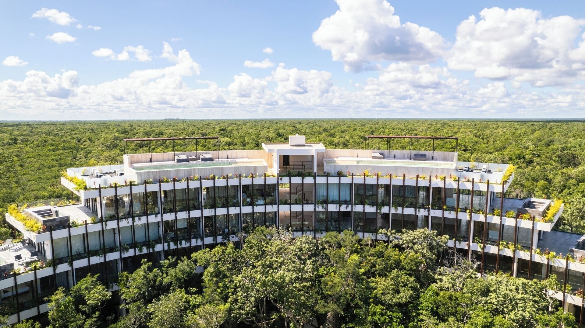 A modern, multi-story building with extensive glass facades, surrounded by lush greenery.