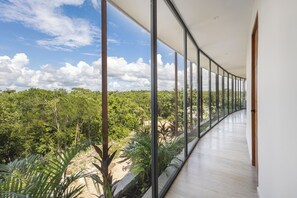 A corridor with large glass windows offering a view of a forested landscape. - Unique penhouse with private pool and jungle view! (Tulum)