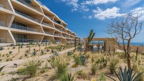 A modern hotel with multiple balconies, desert landscaping, and a view of the ocean. - Bright apartment w/ ocean view and unique decoration (Cabo San Lucas)