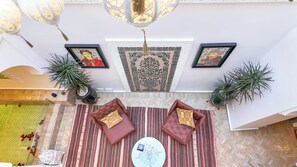 A high-ceilinged lounge area with patterned floor tiles, two cushioned sofas with pillows, a round table, and decorative wall art. - Riad Tamazy  
3-bedroom house in lovely Marrakech with air conditioning (Marrakech)