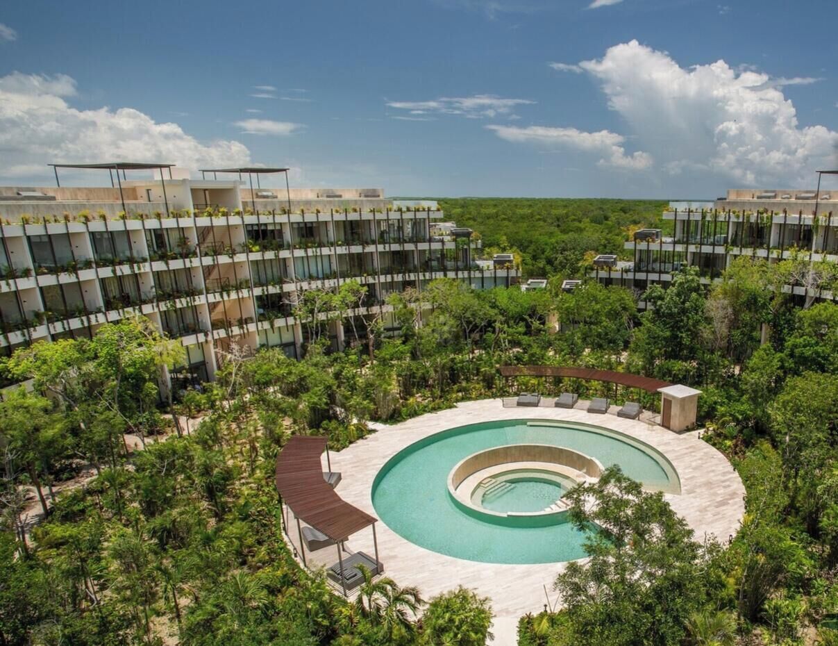 A circular pool surrounded by lush greenery and a modern building in the background.