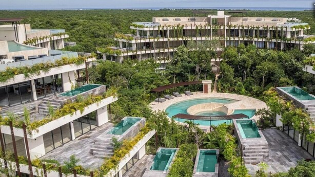 Un complexe hôtelier moderne doté de plusieurs piscines, d’une végétation luxuriante et d’une piscine centrale de forme circulaire, entourée d’espaces de détente.