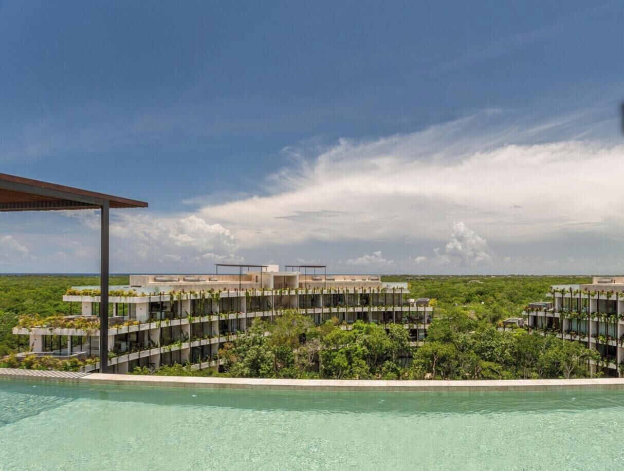 Un hotel modern amb piscina, envoltat de vegetació abundant i un cel clar.