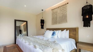 Une chambre à coucher avec une tête de lit en bois, un grand lit avec une literie blanche, un miroir et deux luminaires suspendus.