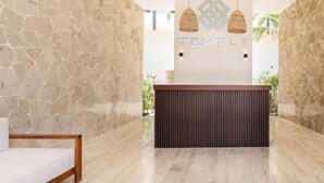 Un espace d’accueil avec un mur en pierre, un comptoir d’accueil en bois et deux lampes suspendues.