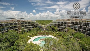 Ein modernes Hotel mit einem zentral gelegenen Pool, umgeben von üppiger Vegetation und mehreren Balkonreihen.