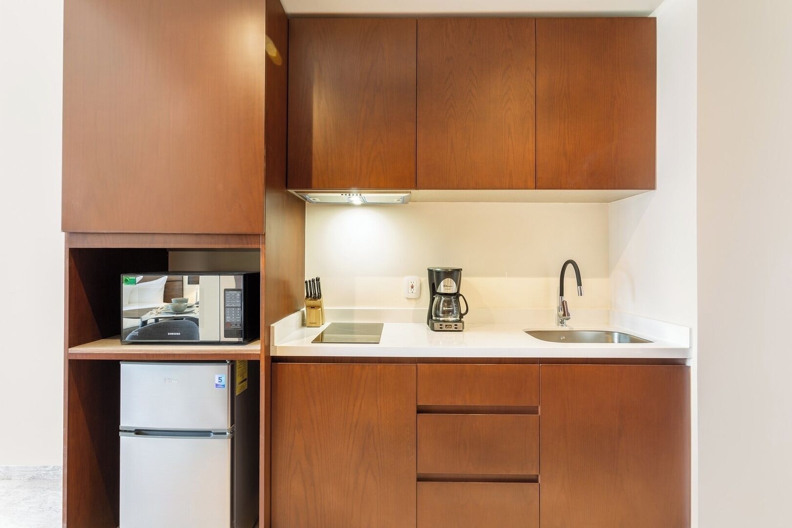 A compact kitchen with wooden cabinets, a built-in microwave, a coffee maker, and a sink.