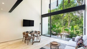 Ein modernes Wohnzimmer mit Essbereich, großen Fenstern und einem Flachbildfernseher.