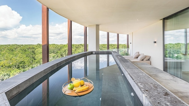 A modern infinity pool with a clear view of the surrounding landscape, a seating area with cushions, and a tray of fruit. - Lavish 3 BD Apartment with Private Pool (Tulum)