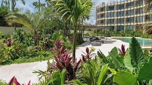 A hotel with a pool, surrounded by lush greenery and a modern building in the background. - Lavish 3 BD Apartment with Private Pool (Tulum)