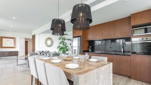 A modern kitchen with wooden cabinets, a built-in oven, and a dining area with a marble table set for six. - Lavish 3 BD Apartment with Private Pool (Tulum)