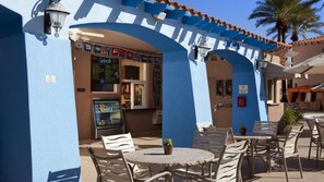 Un'area esterna con tavoli e sedie, una macchina per snack e un edificio con pareti e archi blu.