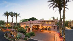 Un hotel in stile mediterraneo con patio, palme e giardino curato.