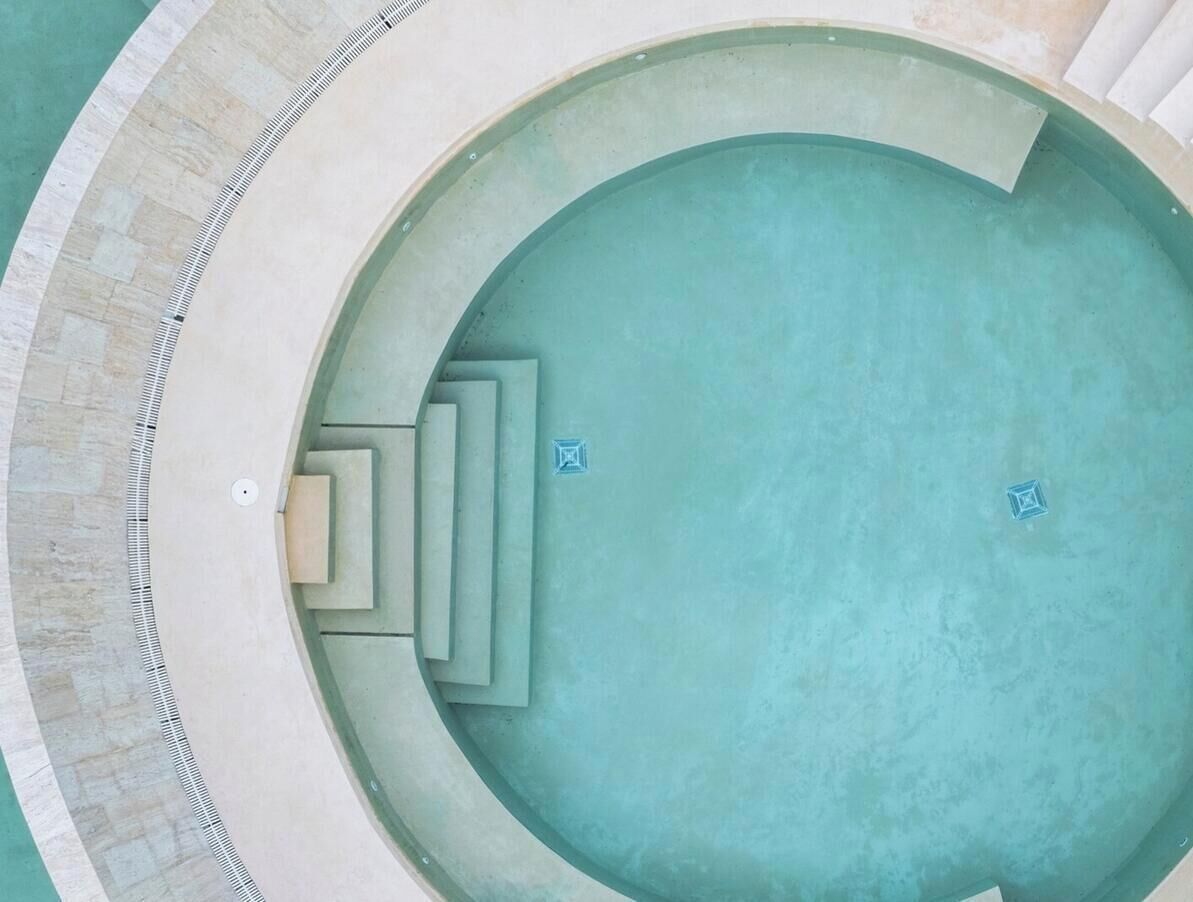 A circular pool with a clear blue water feature, surrounded by a light-colored tiled deck.