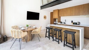 A modern kitchen with wooden cabinets, a white countertop, and a built-in stove. There is a dining area with a wooden table and wicker chairs. - One of a kind! Loft with small pool (Tulum)