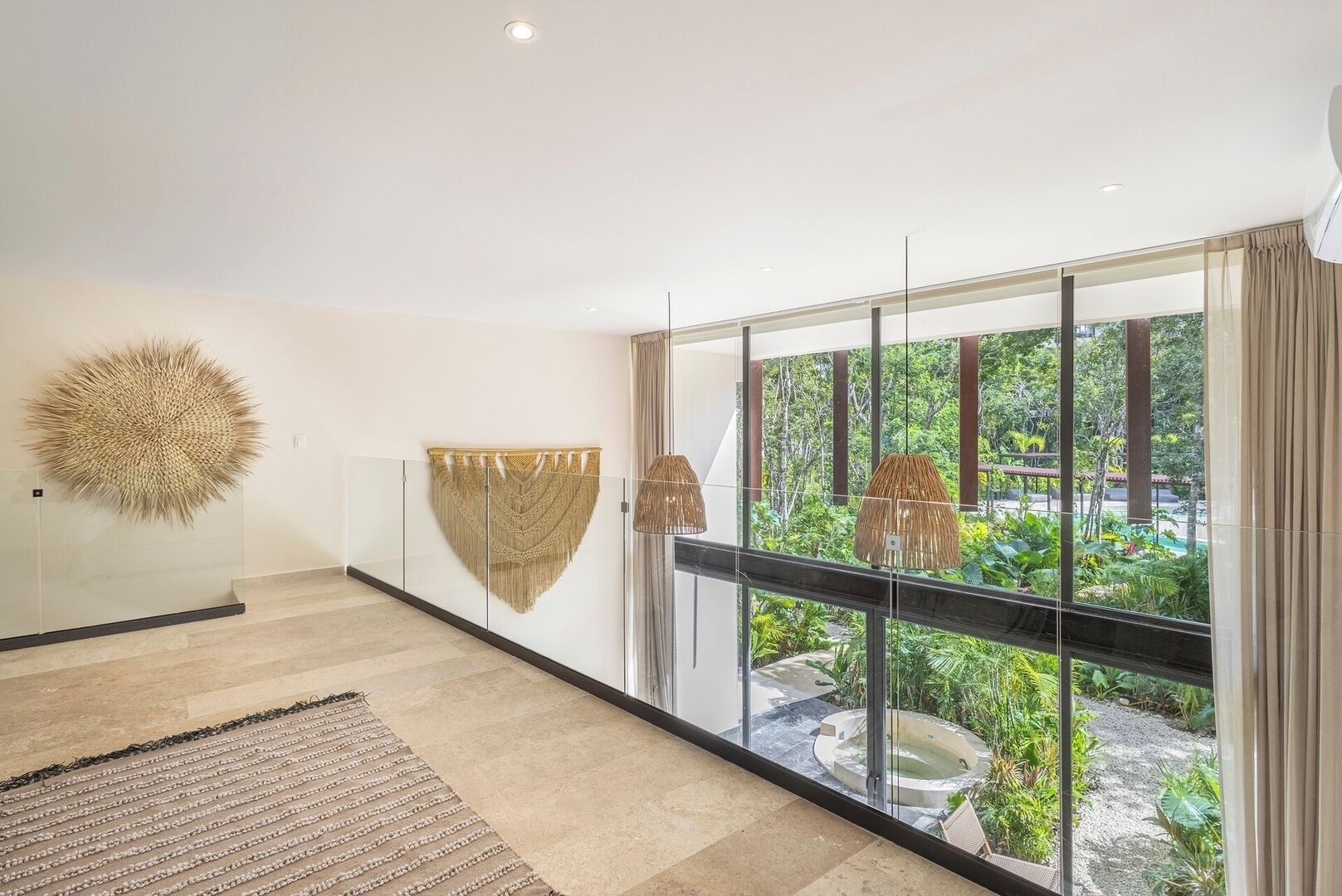 Un intérieur moderne avec un mur en verre, un grand élément décoratif mural et une vue sur un jardin et un jacuzzi à l’extérieur.