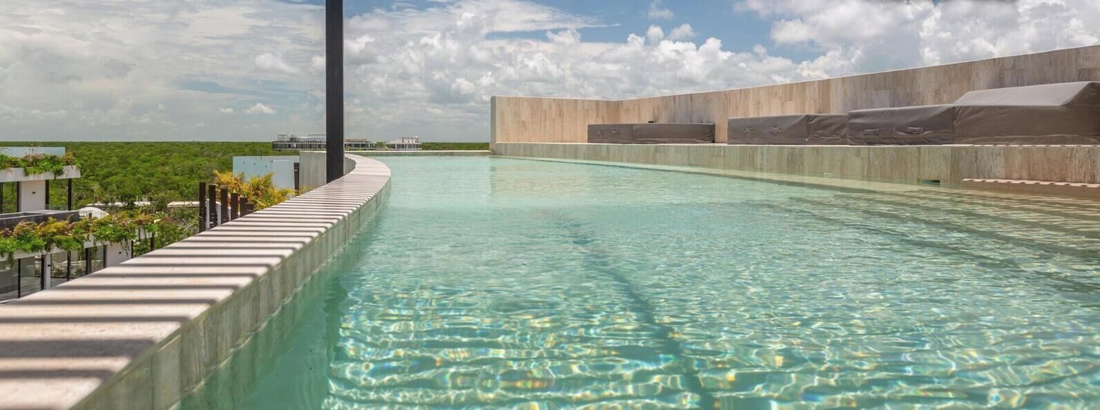 A modern infinity pool with clear water, surrounded by a concrete deck and a tall pillar.