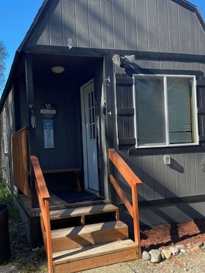 A wooden cabin with a porch, a door, and a window.