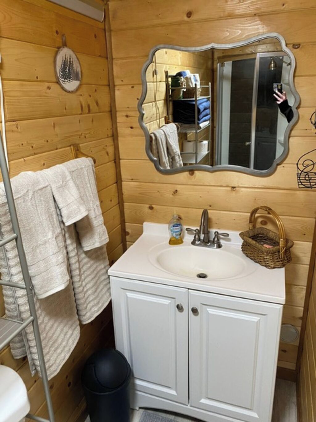 Un baño con paneles de madera, un lavamanos blanco, un espejo y un perchero para toallas.