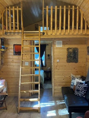 A cabin interior with a loft bedroom, a wooden ladder, a sofa, and a small table.. beautiful rustic cabin 1 bedroom 1 loft 10 min away from prime fishing