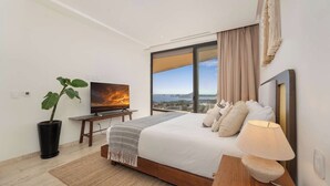 Quarto de hotel moderno com uma cama grande, televisão, planta em vaso e vista para a cidade.