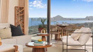 Varanda ampla com vista para o mar e montanhas, mobiliada com sofá, cadeiras e mesa de jantar.