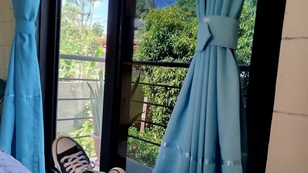 A room with a bed, a window with blue curtains, and a balcony with greenery. - M&K House - KAR Double Room - 1 or 2 beds (Tarapoto)