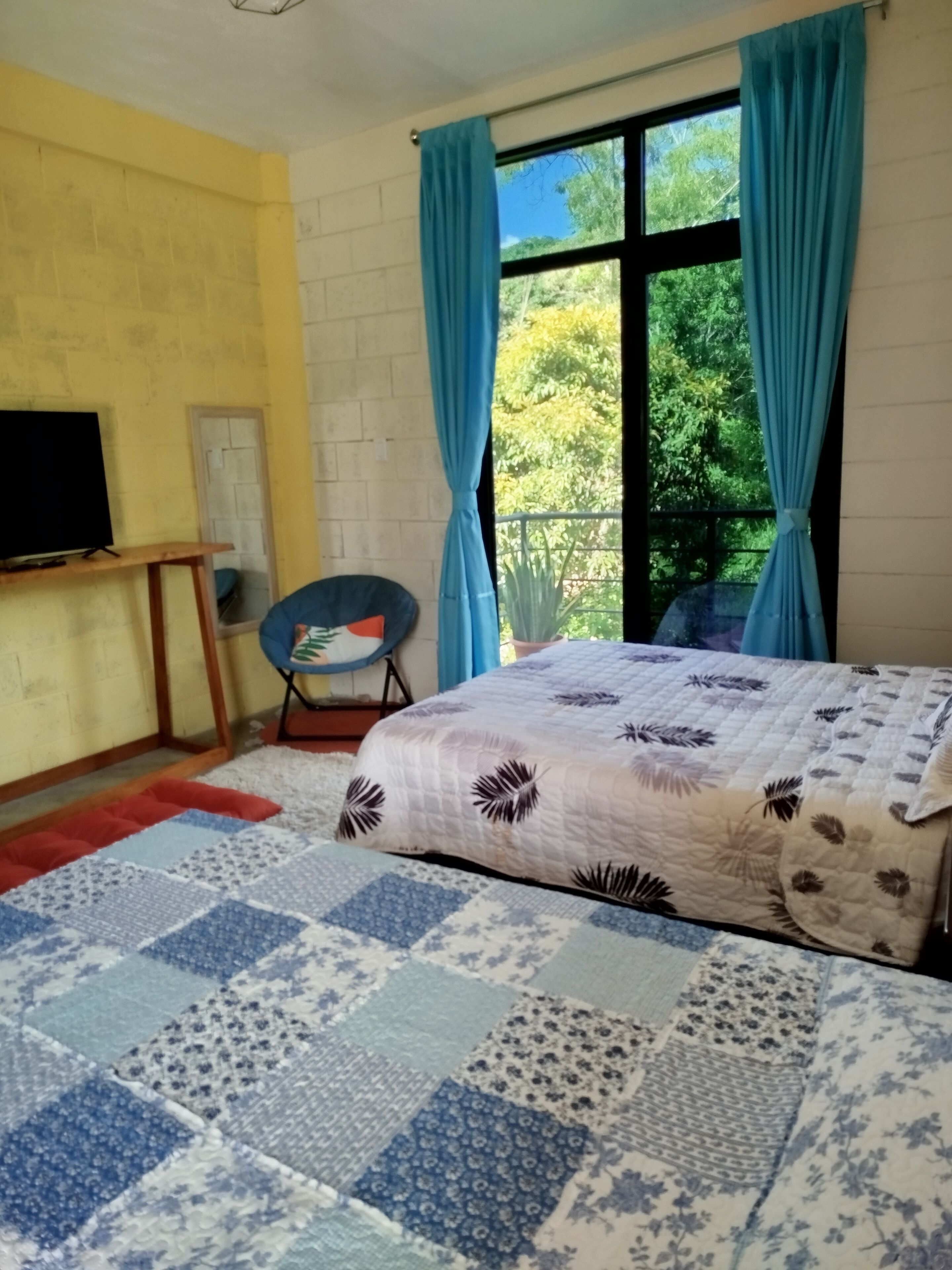 Un dormitorio con cama, una silla, un televisor y una ventana con cortinas.
