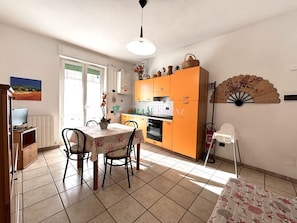 A kitchen with orange cabinets, a dining table with chairs, a TV, and a decorative fan. - Central area close to the beach-Rif. Franco (San Vincenzo)