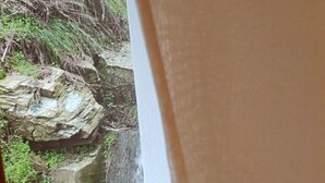 Näköala kivikkoiseen maisemaan ikkunan kautta, jossa verho on osittain vedetty alas.