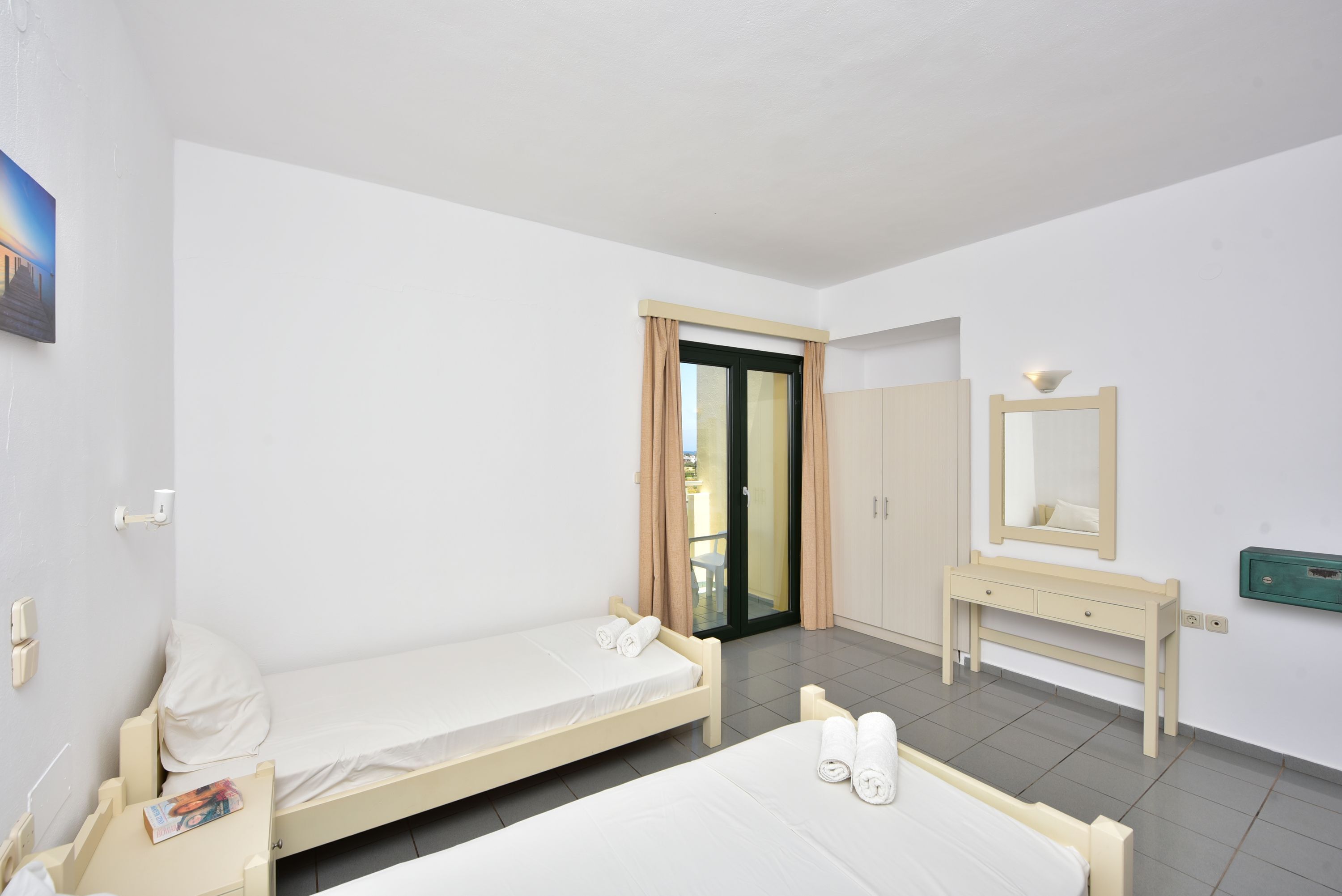 A hotel room with two single beds, a wooden dresser, a mirror, and a door leading to a balcony.