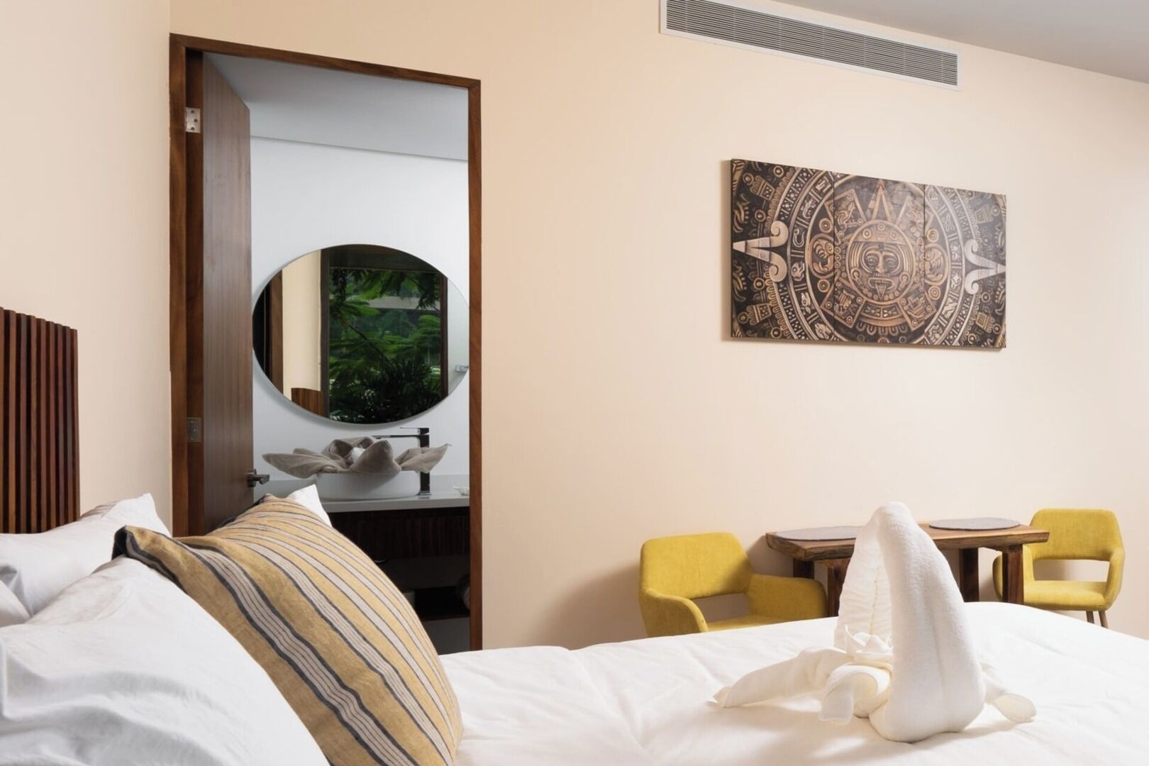 Habitació d'hotel amb un llit, un mirall rodó, escriptori amb cadira i una obra d'art a la paret.
