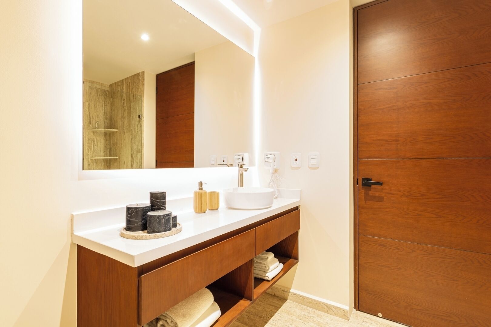 Een moderne badkamer met een witte wastafel, marmeren zeepdispensers, een witte wasbak en een houten deur.