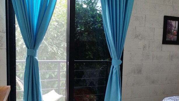 A room with a sliding glass door leading to a balcony, a bed with patterned bedding, and a small potted plant on the floor. - M&K House - Family JUD Room (Tarapoto)
