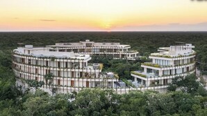 Un complexe hôtelier moderne de forme circulaire, entouré d’une forêt dense, et doté de plusieurs niveaux et de terrasses.