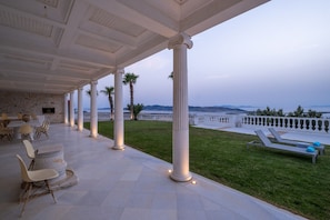 A covered outdoor area with stone flooring, white columns, and a view of the sea. - Luxury Villa Aethra -Island Living Paros- (Παροικιά)